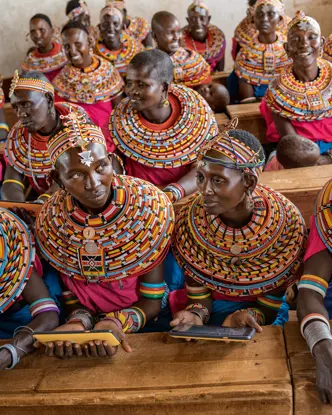Women from the Samburu tribe in Kenya sitting on a wooden bench in traditional clothes and smiling.
