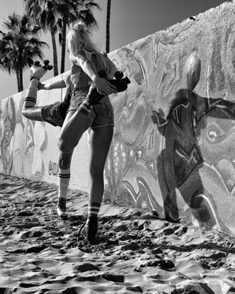A boy looks behind a graffiti-painted wall at two women on roller skates warming up.