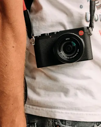 Side shot of a person with a Leica camera hanging in front of his body..