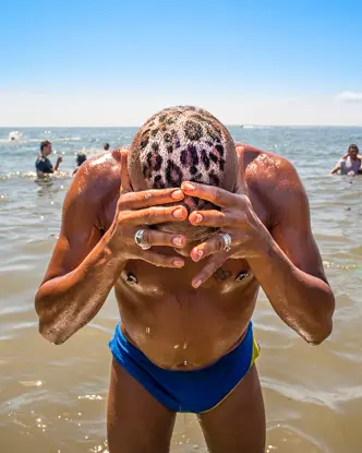 A man with a leopard print on his head is standing in the water. Several people are bathing in the sea around him.