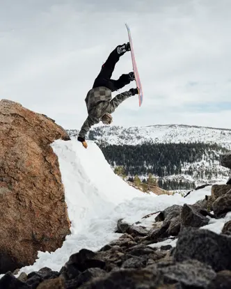 Snowboarder does a one-armed handstand on a ramp in the mountains