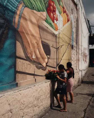 Two women with fruit baskets in front of a big fruit graffiti