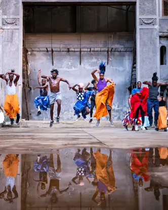 Traditional dancers performing in a historic courtyard in Cuba, captured mid-jump with vibrant costumes and reflections in a rain puddle.