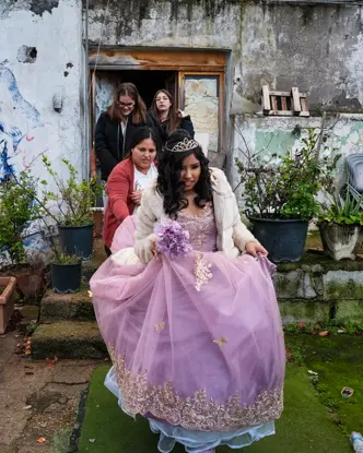 Young woman in a formal quinceañera dress surrounded by family, capturing a milestone celebration within a modest residential setting.