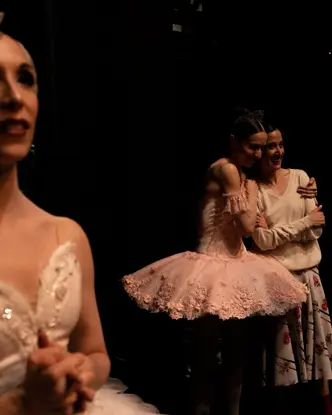 Ballet dancers embracing backstage after a performance while others wait in the wings.