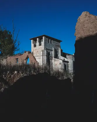 Historic stone ruins and a tower rise from a rugged landscape beneath a deep blue sky, framed by dramatic light and shadow.