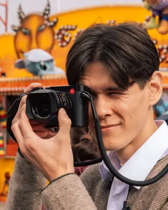 Teo Crawford using a Leica Q3 at Munich Oktoberfest, capturing candid moments in front of a colorful fairground booth during the world's largest folk festival.