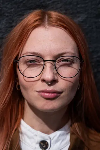 A younger woman with red long hair wears Leica Eyecare glasses.