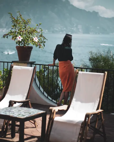 Woman on a large balcony with a view of a lake and mountains.