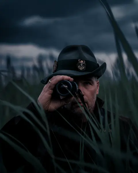 A hunter standing among tall grass at dusk with the Leica Calonox 2 in focus