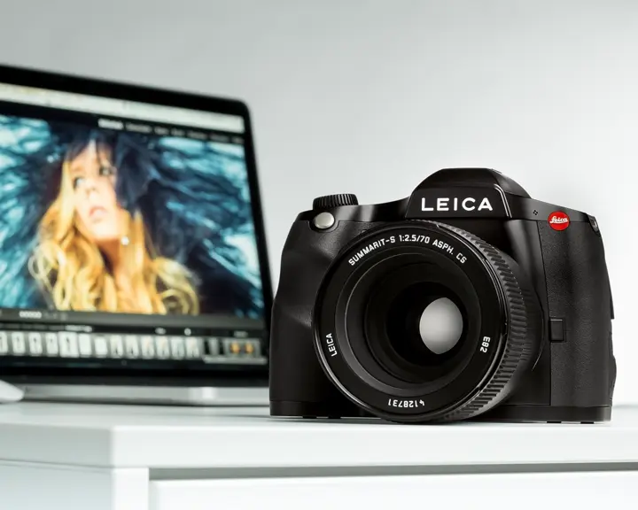 Leica camera on a table in front of a laptop showing a portrait photo.
