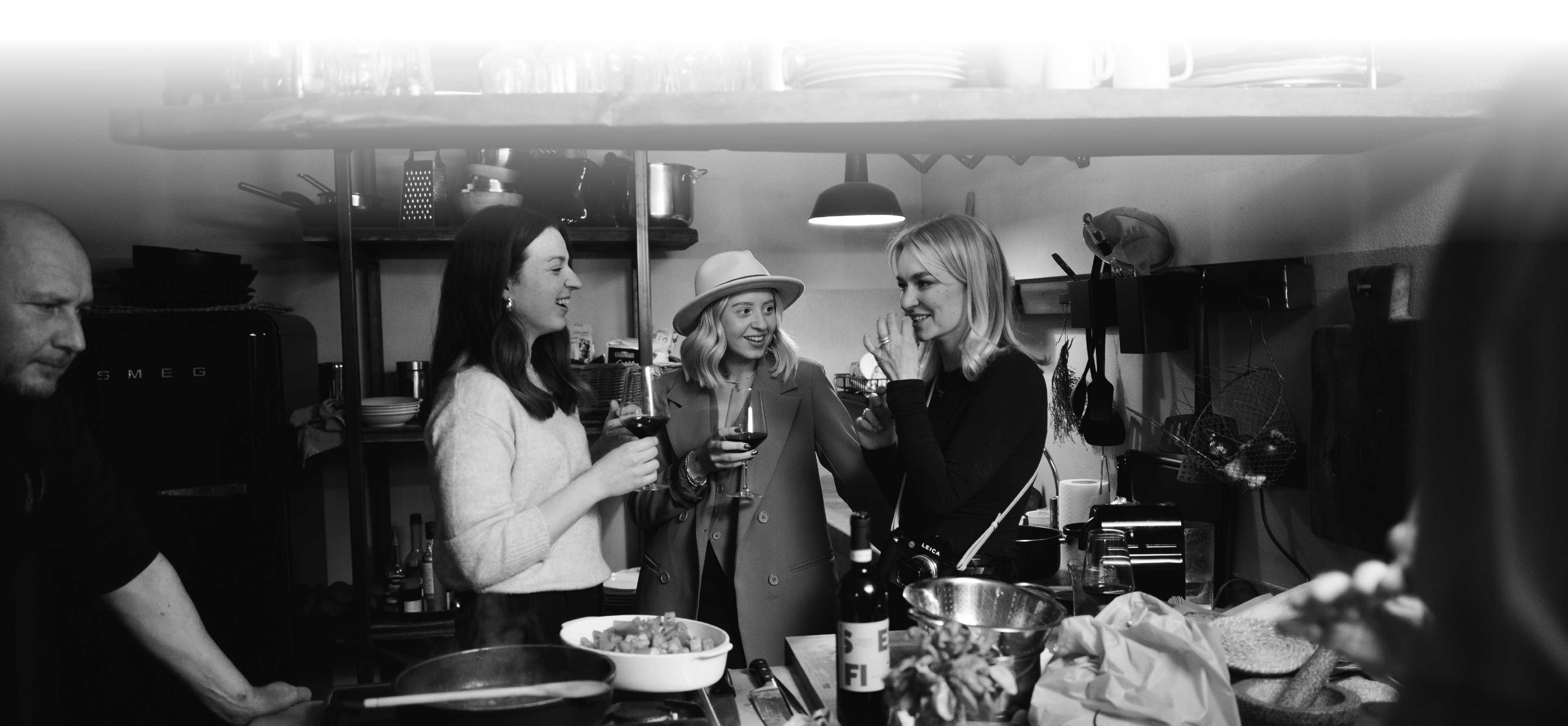 Three women with a wine glass in their hands stand in a kitchen