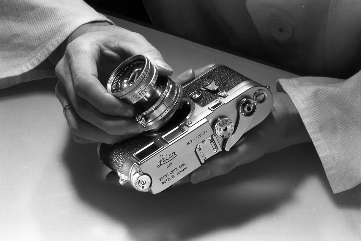 Black and white image of a man putting a lens on a M camera