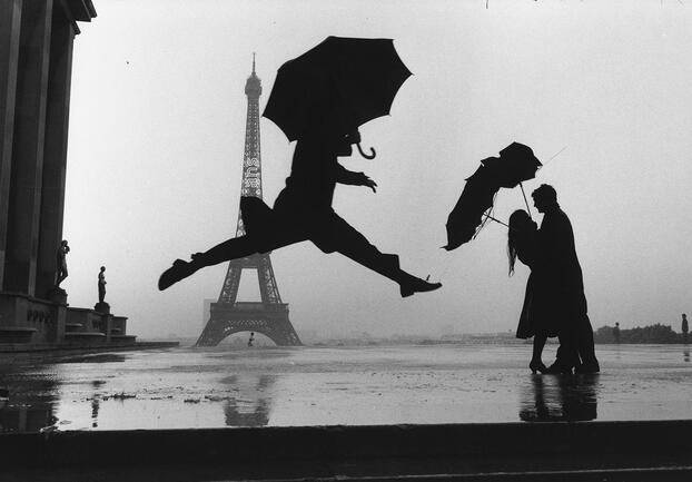 Person jumps in front of the Eiffel Tower with an umbrella.